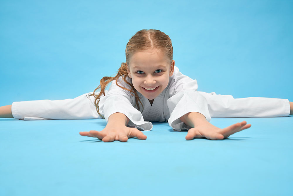 Young girl in karate uniform performing splits and smiling